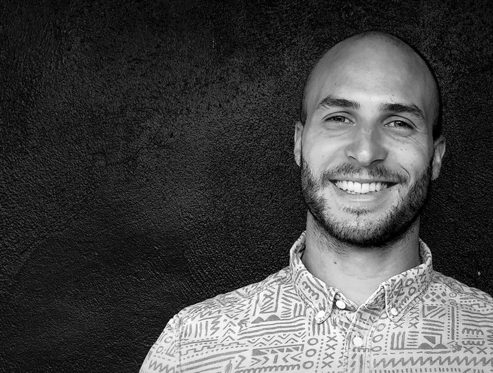 Black and white portrait of a dance instructor posing in front of a dark background.